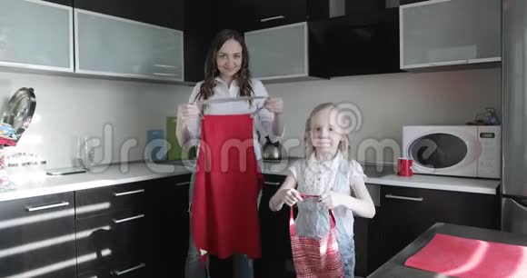 一位年轻的母亲和她的女儿在厨房里穿红色围裙视频的预览图