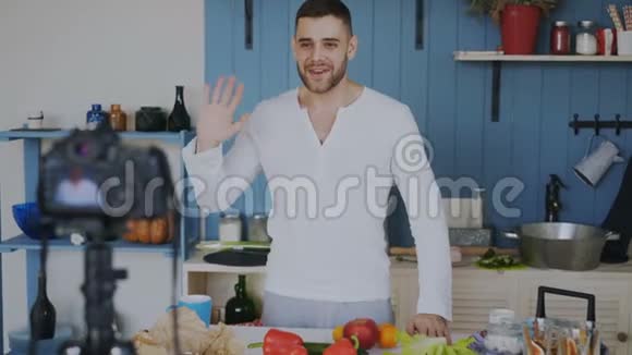 英俊开朗的男人在厨房里用dslr摄像机录制关于烹饪的视频食物博客视频的预览图