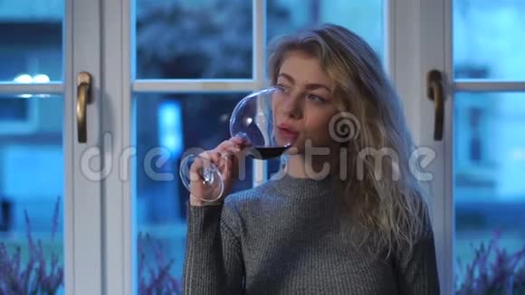 在窗户的背景下喝着红酒时一个闷闷不乐的女孩在一旁看着的特写肖像视频的预览图