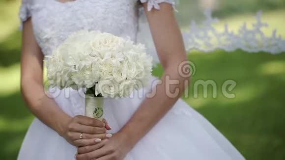 年轻漂亮的新娘穿着婚纱在夏日的公园里放着一束白玫瑰视频的预览图