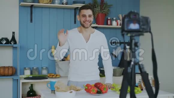 英俊开朗的男人在家厨房的dslr摄像头上录制有关素食健康食品的视频博客视频的预览图