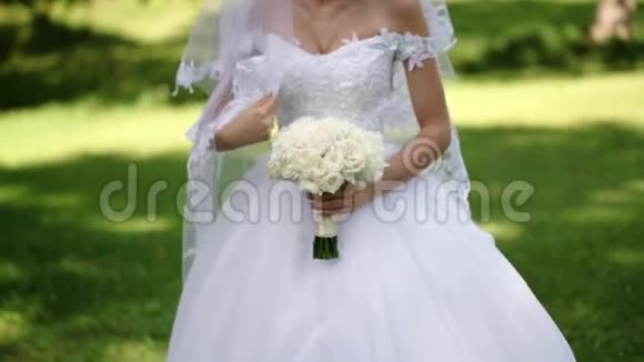 年轻漂亮的新娘穿着婚纱在夏日的公园里放着一束白玫瑰视频的预览图
