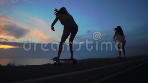 两个女朋友穿着短裤和运动鞋在太阳升起的美丽天空下在斜坡上骑滑板视频的预览图