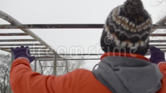 穿橙色夹克的年轻人在冬天在户外的水平杆上做拉力视频的预览图