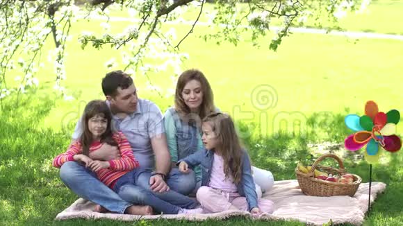 一个年轻家庭的肖像父母把时间花在户外在一棵盛开的苹果树下野餐视频的预览图