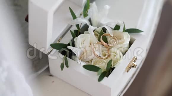 两个金色结婚戒指放在一个白色的木箱里里面放着玫瑰花视频的预览图