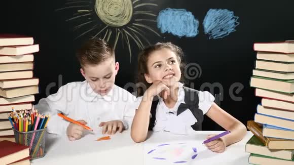 回到学校的概念孩子们坐在一张桌子旁桌上放着一堆书黑板后面放着孩子们的图画男孩视频的预览图