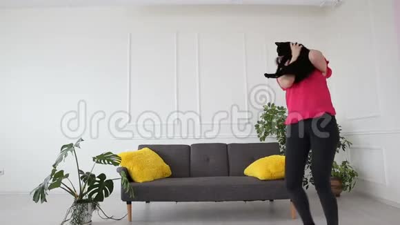 对宠物的爱漂亮的黑发女孩和一只黑猫在客厅的家里跳舞视频的预览图