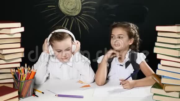 回到学校的概念男孩和女孩坐在书桌前桌上放着一大堆书黑板后面放着孩子们的图画视频的预览图