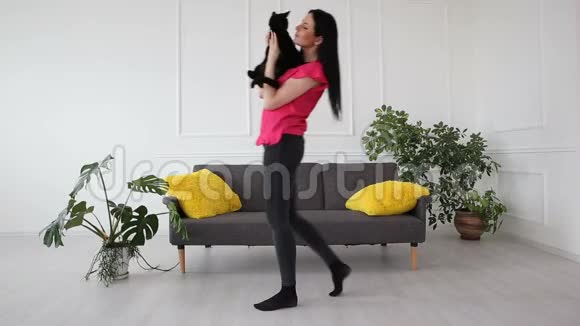 对宠物的爱漂亮的黑发女孩和一只黑猫在客厅的家里跳舞视频的预览图