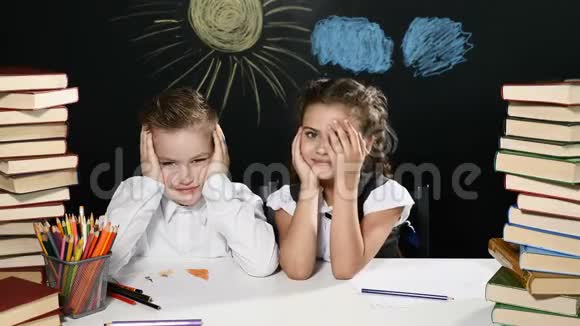 回到学校的概念男孩和女孩坐在一张桌子前桌子后面有一堆书和一块黑板上面有图纸儿童视频的预览图
