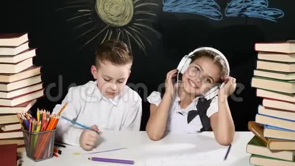 回到学校的概念男孩和女孩坐在书桌前桌上放着一大堆书黑板后面放着孩子们的图画视频的预览图
