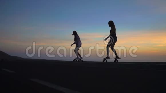 两个女朋友穿着短裤和运动鞋在太阳升起的美丽天空下在斜坡上骑滑板视频的预览图
