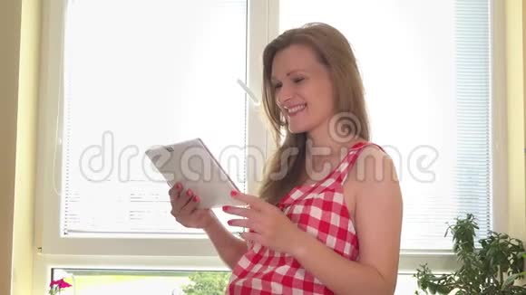 幸福的孕妇带着平板电脑挑选蔬菜沙拉的食谱视频的预览图