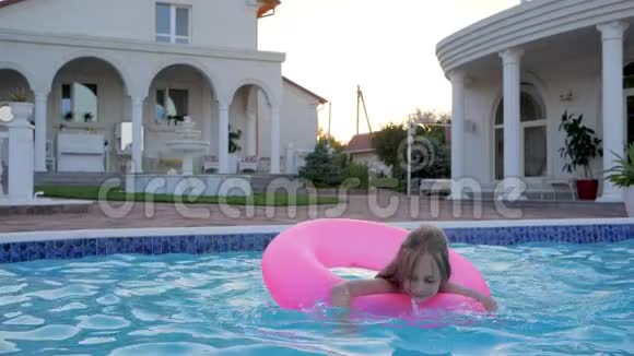 美丽的小女孩在游泳池的充气粉红戒指上游泳在大厦的暑假泼水视频的预览图
