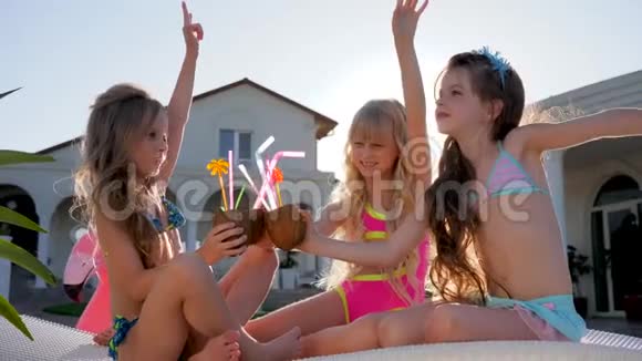 穿着泳衣的小女孩在别墅附近的背光区玩得很开心有钱的孩子在日光浴床上手里拿着椰子鸡尾酒在户外视频的预览图