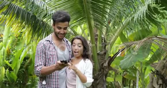 情侣用手机拥抱在棕榈树上交谈年轻人和女人在网上聊天快乐的微笑视频的预览图
