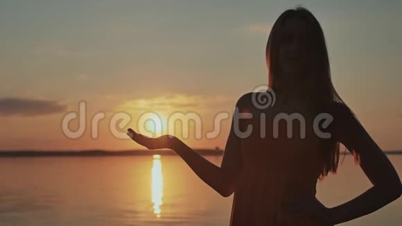 这个年轻的女孩把太阳从她的手中释放出来美丽浪漫的日落视频的预览图
