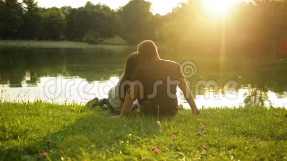 两个情人在美丽的日落中亲吻坐在城市公园的湖边在外面看到幸福夫妇视频的预览图