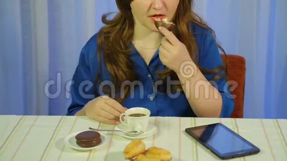 一个女人在一张桌子旁的咖啡馆里喝着咖啡和甜点读着平板电脑上的新闻视频的预览图