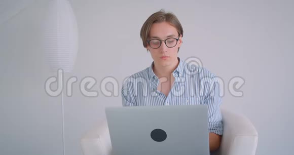 年轻有魅力的高加索商人用笔记本电脑坐在室内扶手椅上的特写照片视频的预览图