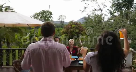 一对夫妇带着果汁人们在露台上传递食物年轻的朋友坐在桌子上聊天交流视频的预览图