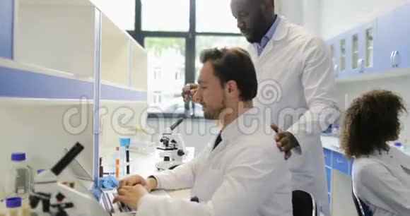 在现代实验室工作的不同的科学家小组两位男性同事讨论试管中的例子视频的预览图