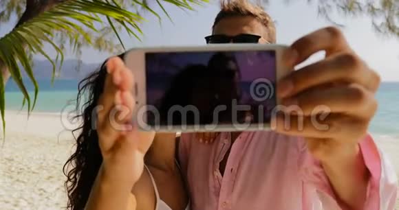 情侣在沙滩亲吻手机上自拍快乐的微笑男人和女人在爱中巡回视频的预览图