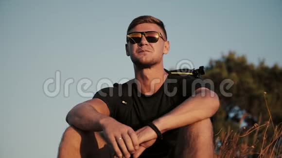 慢动作的英俊年轻时尚男子戴着太阳镜和背包看着夕阳在田野1920x1080特写视频的预览图