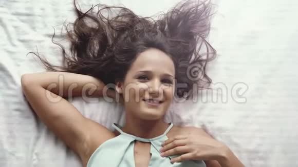 俯视着年轻的白种人美女看着镜头微笑躺在床上的快乐女孩慢动作视频的预览图