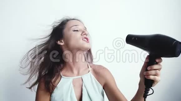 美丽的年轻快乐的女人在白色背景上使用吹风机唱歌慢动作3840x2160视频的预览图