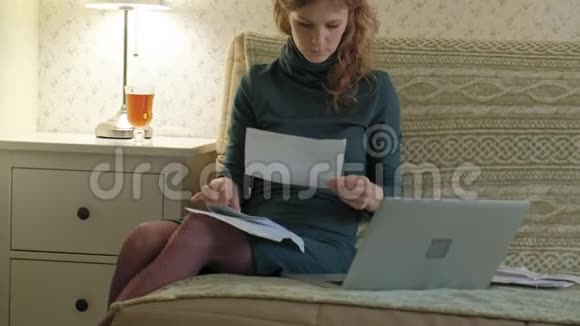 年轻女子穿着绿色连衣裙坐在沙发上手提电脑工作学习文件在家工作视频的预览图
