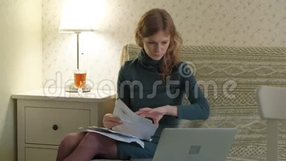 年轻女子穿着绿色连衣裙坐在沙发上手提电脑工作学习文件在家工作视频的预览图