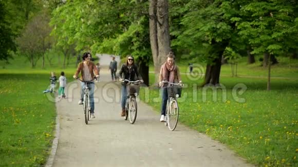三位活跃的年轻妇女一起在城市公园骑马带着自行车在户外微笑的布鲁内特视频的预览图