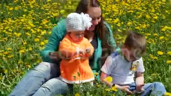 一个快乐的孩子和他的家人在蒲公英的春天的小路上和姐姐和妈妈一起在绿色上翻滚很有趣视频的预览图