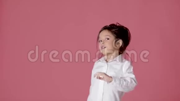 穿着白色衬衫在粉红色背景上跳舞的小女孩视频的预览图