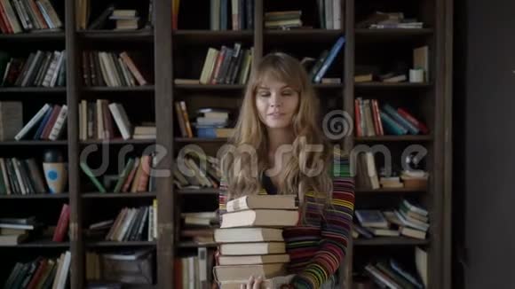 年轻漂亮的女孩拿着一叠书在书架前视频的预览图