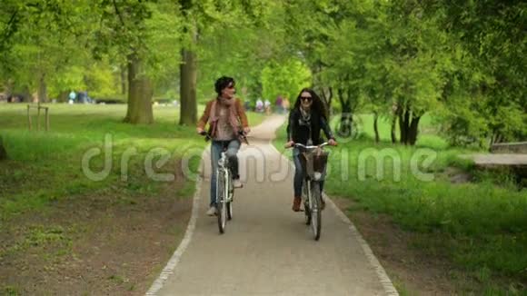 两个黑发女人正骑着车穿过城市公园美丽的带自行车的不伦带车享受温暖的阳光视频的预览图