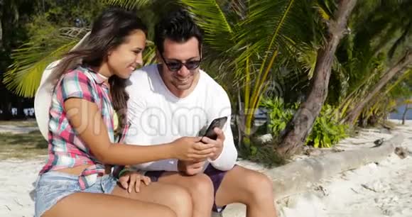 情侣在棕榈树下的手机智能手机户外快乐的微笑男人和海滩上的女人视频的预览图
