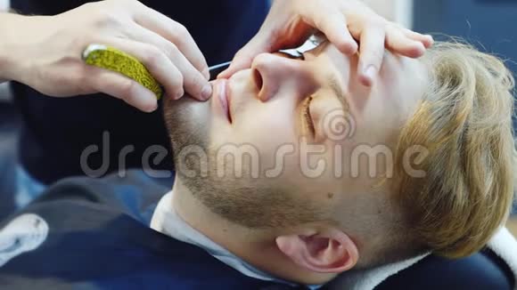 一个年轻人在理发店用危险的剃刀刮胡子视频的预览图