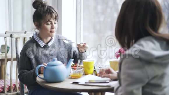 两个年轻的大学生女孩在咖啡馆里吃饭一边说话视频的预览图