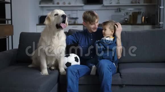 父亲带着蹒跚学步的儿子和狗坐在沙发上视频的预览图