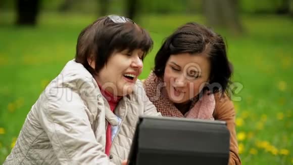 成熟的黑发女人正在平板电脑屏幕上向她笑的母亲展示一些东西快乐的家庭花时间视频的预览图