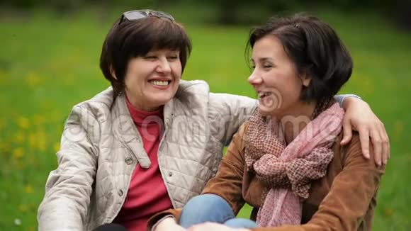 在公园野餐时两个满脸笑容的黑发女人正坐在毯子上互相交谈肖像视频的预览图