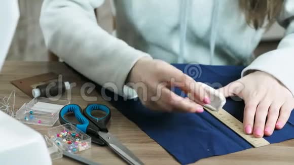特写的手缝在桌子上用尺子和粉笔在蓝色织物上切割视频的预览图