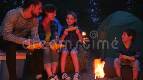 夏令营带孩子的年轻父母在露营地度假吃玉米和喝啤酒幸福的家庭吃视频的预览图