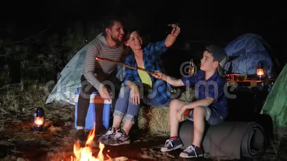 爸爸妈妈带着儿子在篝火旁的大自然中的android上拍照幸福的家庭在手机上拍照视频的预览图