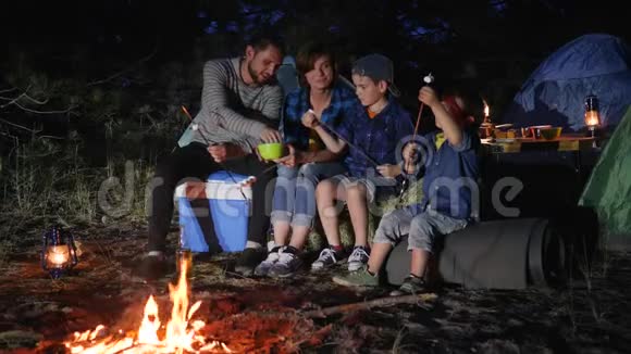 夫妻俩带着孩子在林地的篝火旁放羊肉串家人交流视频的预览图