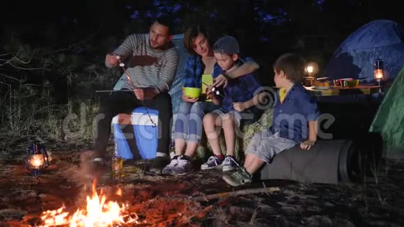 露营地家庭交流把棉花糖放在森林里的火堆上丈夫和妻子视频的预览图