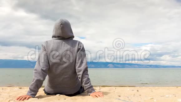 电影摄影男人或女人坐在海滩上的帽衫里后景4k视频的预览图